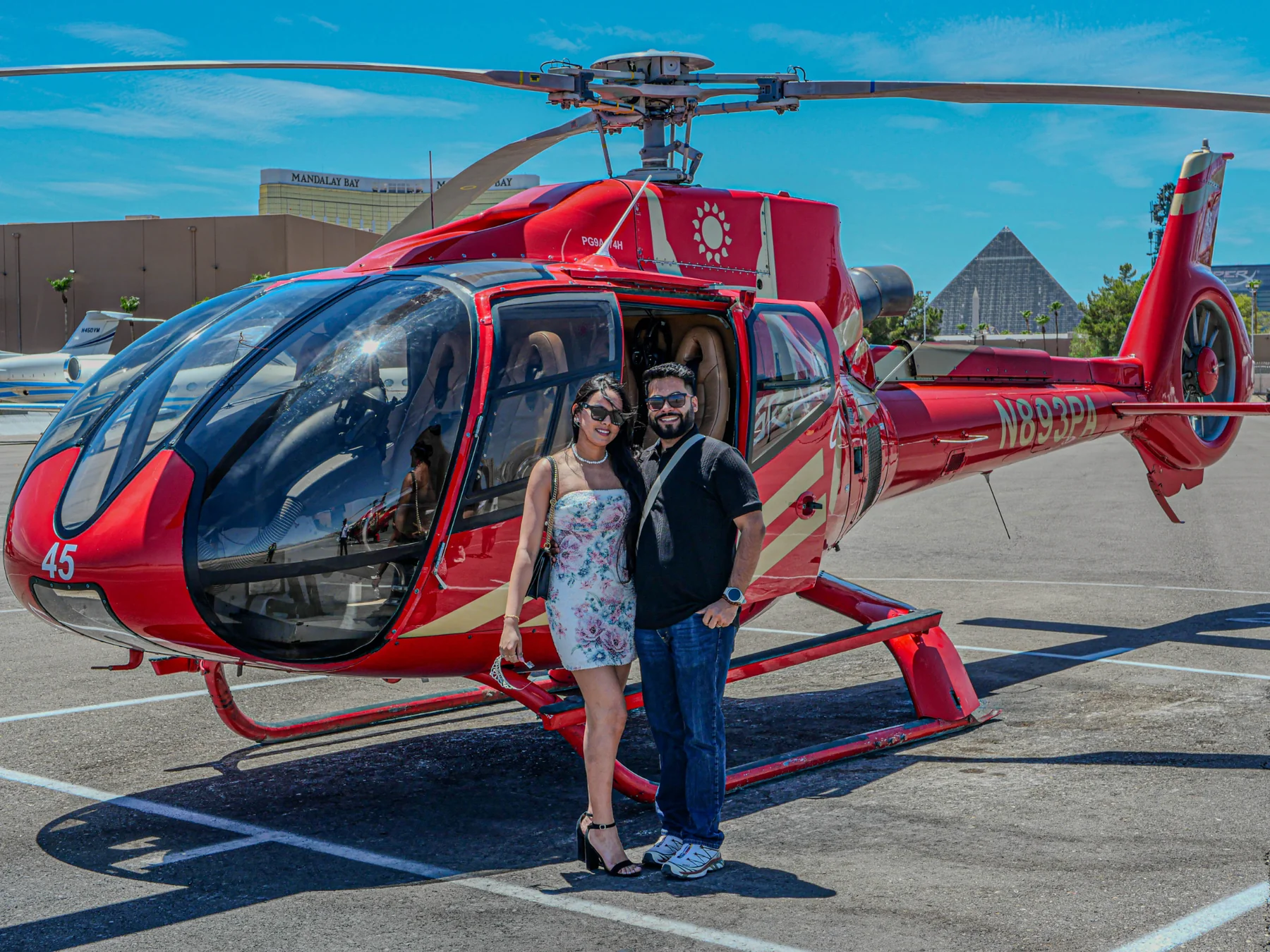 Two creators standing beside a red sightseeing helicopter in Las Vegas